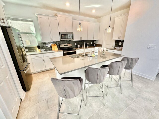 kitchen with appliances with stainless steel finishes, decorative light fixtures, white cabinets, and a breakfast bar