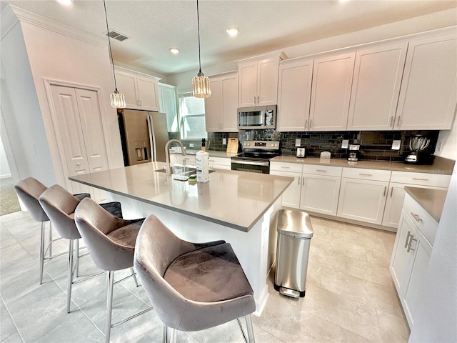 kitchen with decorative light fixtures, a kitchen island with sink, stainless steel appliances, sink, and white cabinetry