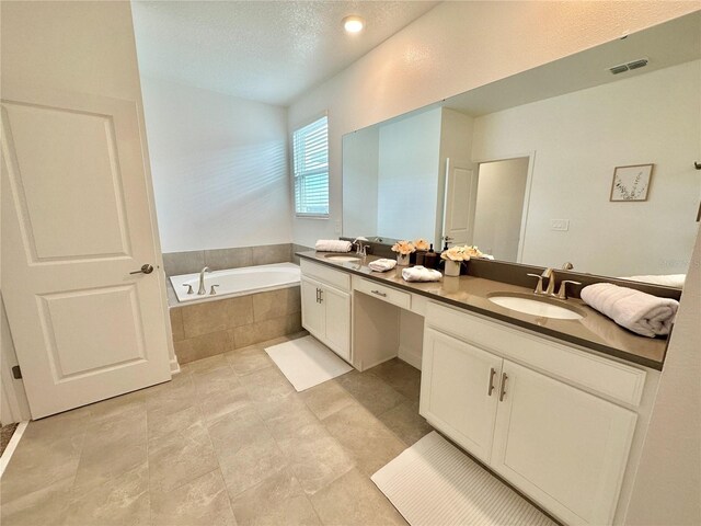 bathroom with a textured ceiling, tiled bath, and vanity