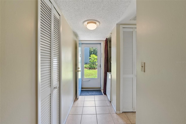 doorway to outside with a textured ceiling, washer / clothes dryer, and light tile patterned floors