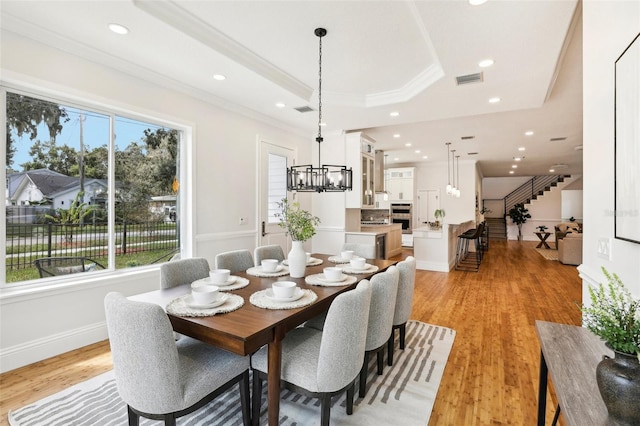 dining space with light wood-type flooring, a healthy amount of sunlight, a tray ceiling, and crown molding