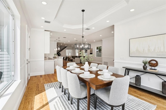 dining room featuring a notable chandelier, a tray ceiling, light hardwood / wood-style floors, and crown molding