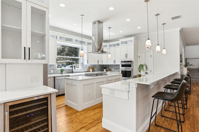 kitchen featuring appliances with stainless steel finishes, white cabinetry, wine cooler, island range hood, and a kitchen island