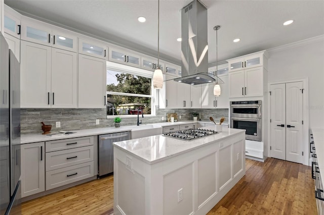 kitchen with appliances with stainless steel finishes, hanging light fixtures, white cabinets, a kitchen island, and light hardwood / wood-style flooring