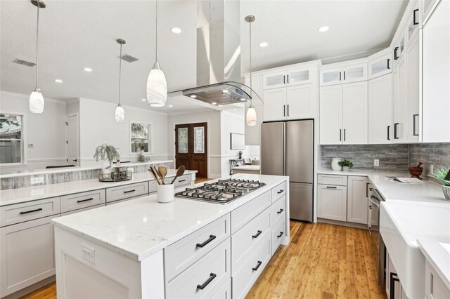 kitchen featuring white cabinets, island range hood, stainless steel appliances, a center island, and decorative light fixtures