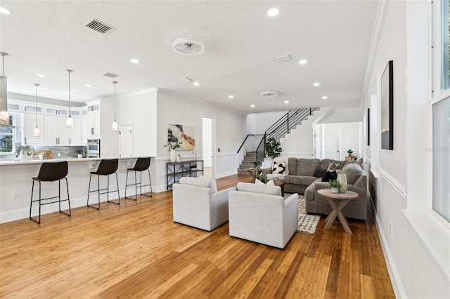 living room with a textured ceiling, light wood-type flooring, and crown molding