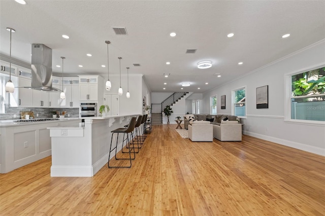 kitchen featuring hanging light fixtures, island exhaust hood, white cabinetry, stainless steel appliances, and light hardwood / wood-style floors