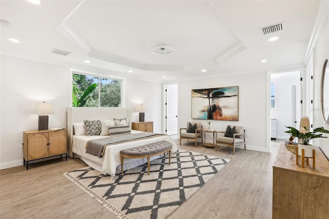 bedroom featuring light wood-type flooring, connected bathroom, a tray ceiling, and crown molding