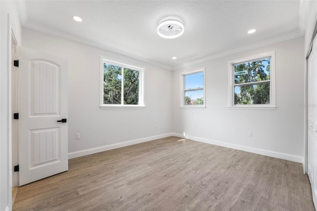 empty room featuring a textured ceiling, light hardwood / wood-style flooring, and ornamental molding