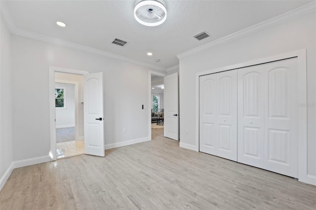 unfurnished bedroom featuring a closet, a textured ceiling, light hardwood / wood-style floors, and crown molding