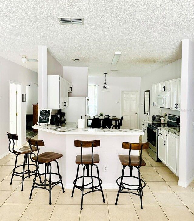 kitchen with a kitchen bar, kitchen peninsula, white appliances, and a textured ceiling