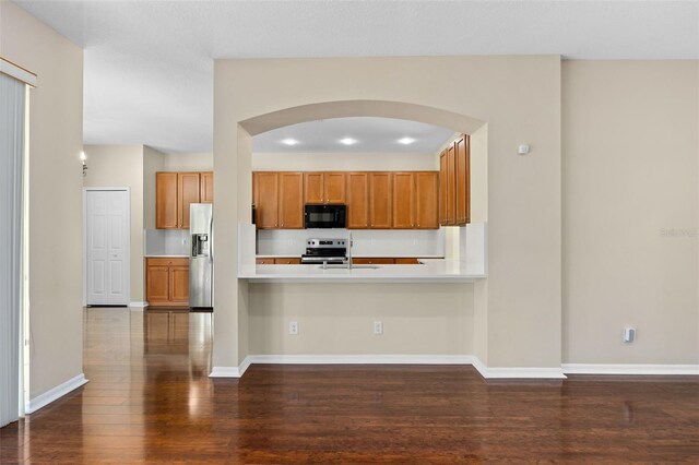 kitchen with appliances with stainless steel finishes, kitchen peninsula, and dark hardwood / wood-style floors