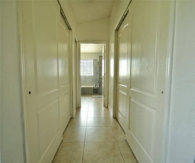 corridor featuring vaulted ceiling and light tile patterned flooring