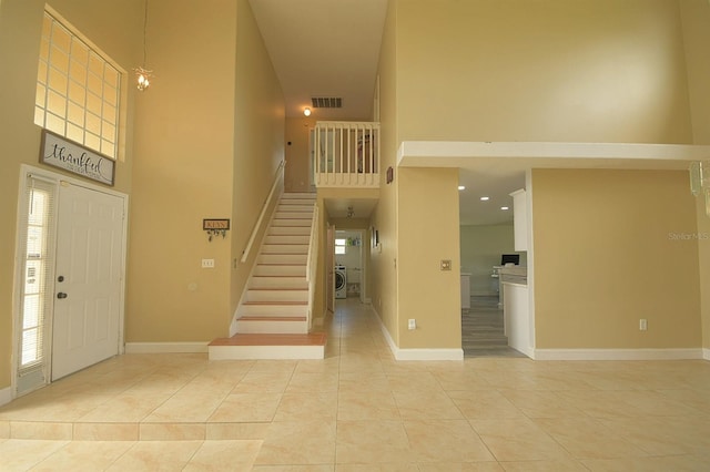 foyer entrance featuring washer / dryer, a high ceiling, light tile patterned flooring, and a notable chandelier