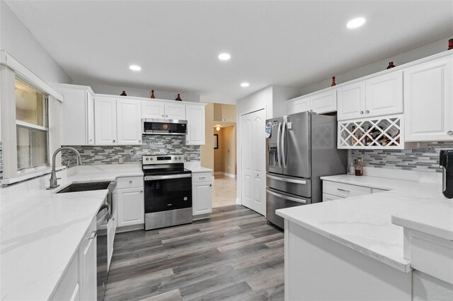 kitchen with appliances with stainless steel finishes, sink, light stone counters, and white cabinets