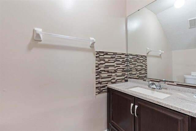 bathroom featuring tile walls, toilet, vanity, and lofted ceiling