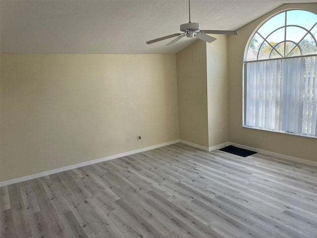 empty room with lofted ceiling, ceiling fan, light wood-type flooring, and a textured ceiling