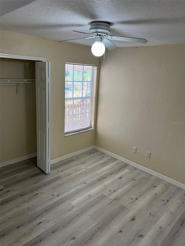 unfurnished bedroom featuring light wood-type flooring, a closet, ceiling fan, and a textured ceiling