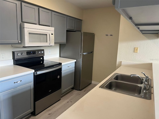 kitchen with light wood-type flooring, appliances with stainless steel finishes, gray cabinets, and sink