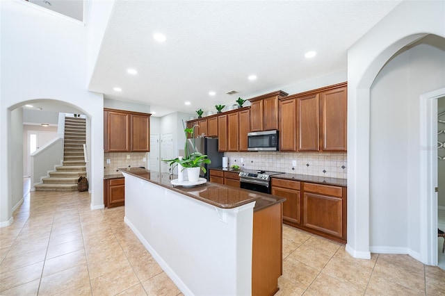 kitchen with a center island with sink, light tile patterned floors, stainless steel appliances, and tasteful backsplash