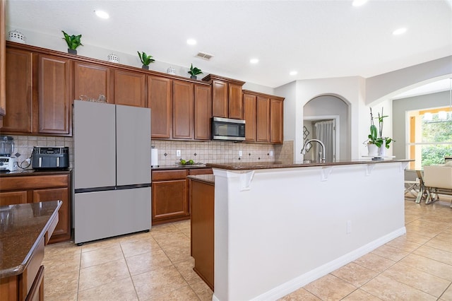 kitchen with light tile patterned flooring, tasteful backsplash, white fridge, a kitchen bar, and a center island with sink