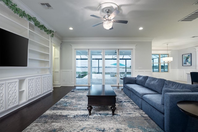 living room with ceiling fan with notable chandelier, crown molding, dark wood-type flooring, and built in features