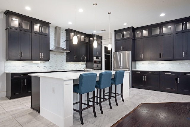 kitchen with sink, wall chimney exhaust hood, decorative backsplash, a center island with sink, and decorative light fixtures