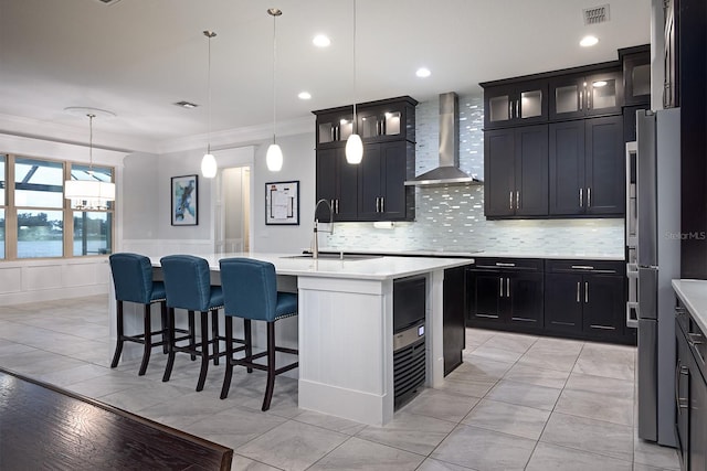 kitchen with an island with sink, sink, decorative light fixtures, wall chimney range hood, and crown molding