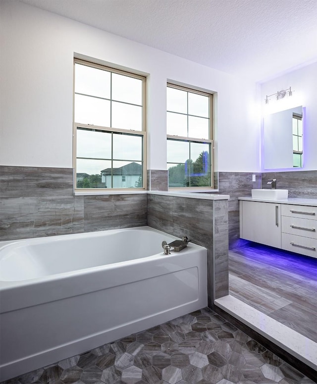 bathroom with tile walls, vanity, a textured ceiling, and a bathtub