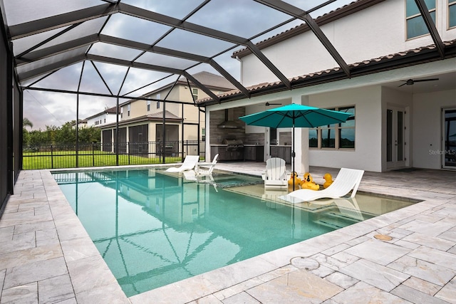 view of swimming pool with a patio, glass enclosure, ceiling fan, and exterior kitchen