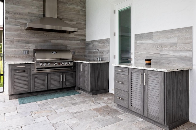 kitchen with light stone countertops, wall chimney exhaust hood, sink, and tile walls