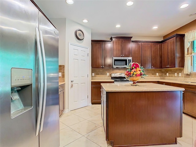 kitchen with appliances with stainless steel finishes, tasteful backsplash, a kitchen island, light stone countertops, and light tile patterned floors