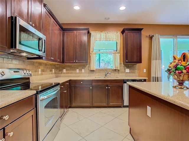 kitchen featuring appliances with stainless steel finishes, tasteful backsplash, light stone countertops, light tile patterned floors, and sink