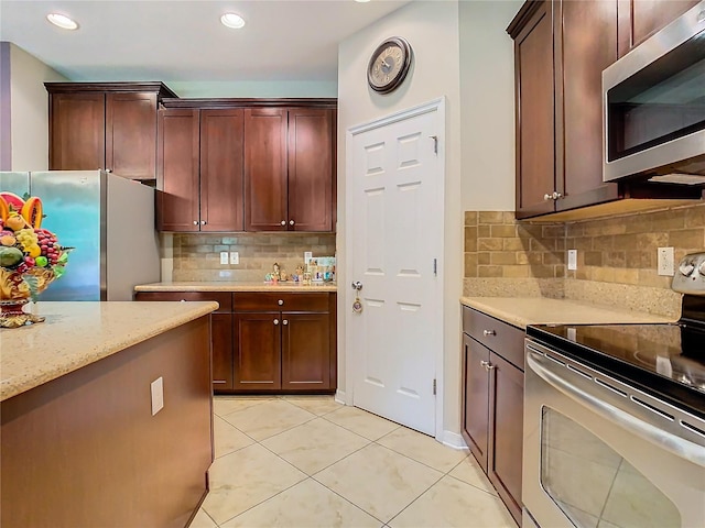 kitchen with appliances with stainless steel finishes, backsplash, light stone countertops, and light tile patterned floors