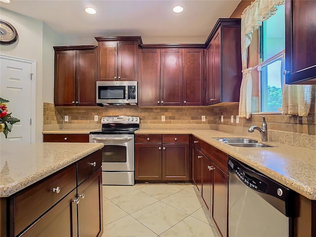 kitchen with appliances with stainless steel finishes, light stone countertops, sink, and tasteful backsplash