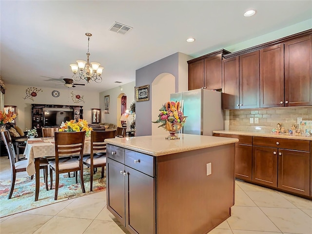 kitchen with hanging light fixtures, stainless steel fridge, tasteful backsplash, a center island, and ceiling fan with notable chandelier