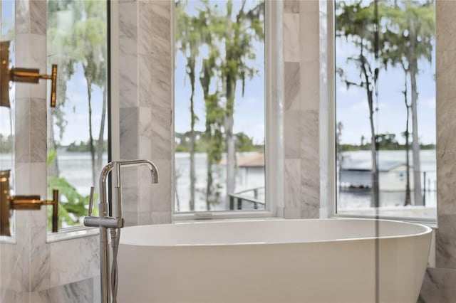 bathroom with a washtub, a water view, and tile walls