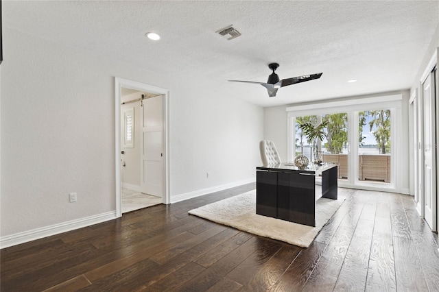 home office with a barn door, ceiling fan, dark hardwood / wood-style flooring, and a textured ceiling