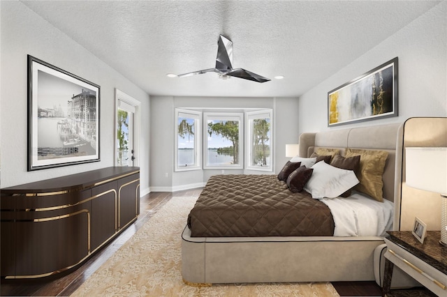 bedroom featuring ceiling fan, light hardwood / wood-style floors, and a textured ceiling