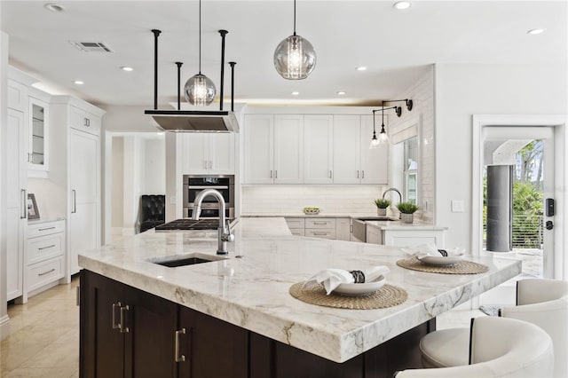 kitchen with a sink, decorative backsplash, visible vents, and stainless steel oven