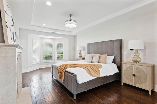 bedroom featuring baseboards, dark wood finished floors, a tray ceiling, recessed lighting, and a fireplace