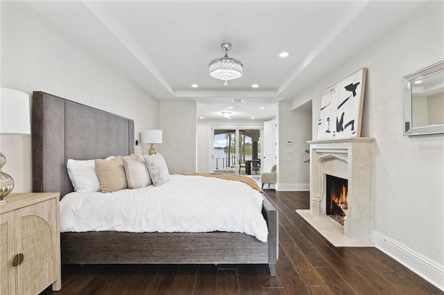 bedroom featuring a raised ceiling, dark wood-style floors, a high end fireplace, recessed lighting, and baseboards