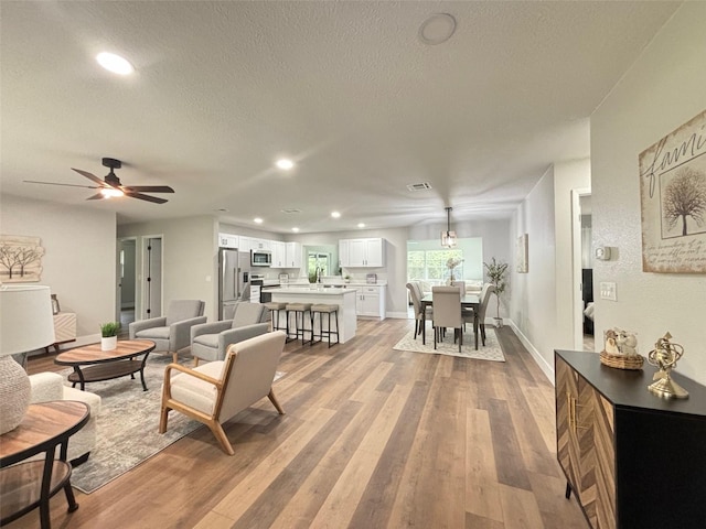 living room with light wood-type flooring, ceiling fan, and a textured ceiling