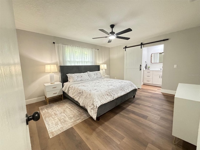 bedroom with ensuite bathroom, a barn door, dark wood-type flooring, ceiling fan, and a textured ceiling