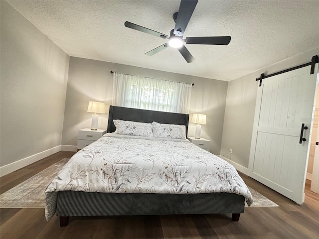 bedroom with a textured ceiling, a barn door, ceiling fan, and dark hardwood / wood-style flooring