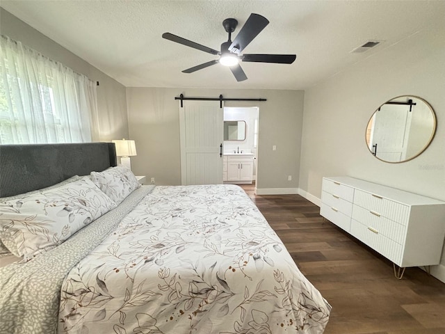 bedroom featuring a textured ceiling, dark hardwood / wood-style flooring, ceiling fan, ensuite bathroom, and a barn door