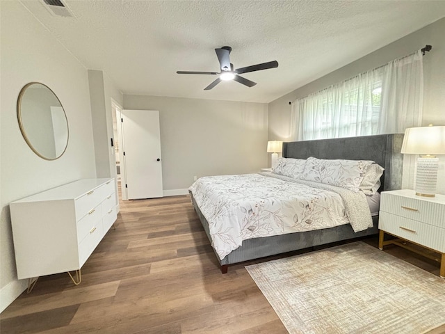 bedroom with hardwood / wood-style floors, ceiling fan, and a textured ceiling