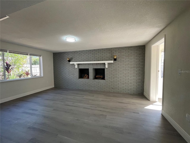 unfurnished living room featuring wood-type flooring, a fireplace, brick wall, and a textured ceiling