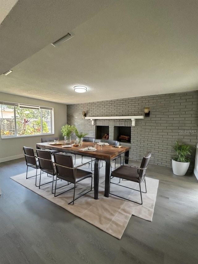 dining area with hardwood / wood-style floors, a fireplace, brick wall, and a textured ceiling