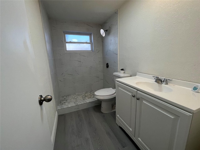 bathroom with hardwood / wood-style floors, toilet, tiled shower, and vanity